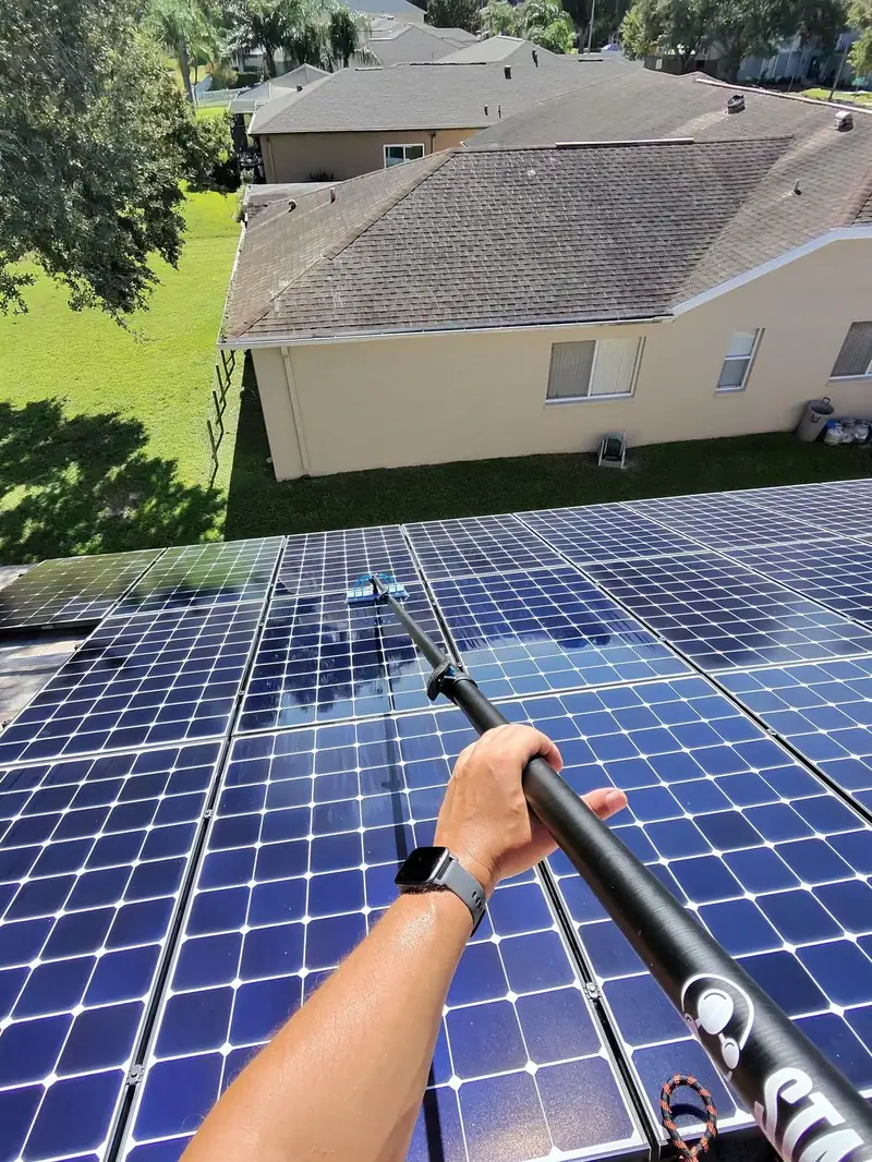 Technician cleaning solar panels with a water-fed pole
